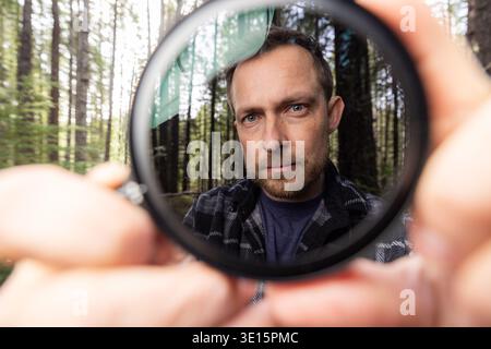 Man smiles through a neutral density filter for the camera . Green trees blur behind his face. Natural light filters through the canopy. He holds the Stock Photo