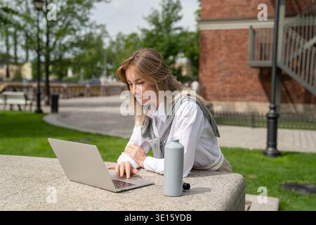 Focused positive businesswoman working on laptop outdoors, enjoying remote work on fresh air. Stock Photo