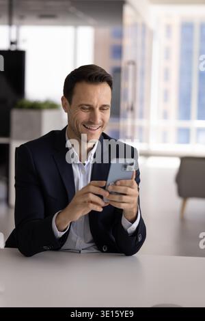 Smiling Hispanic office employee checking smartphone at workplace desk Stock Photo