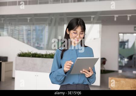 Focused Chinese business professional woman in glasses typing on tablet Stock Photo