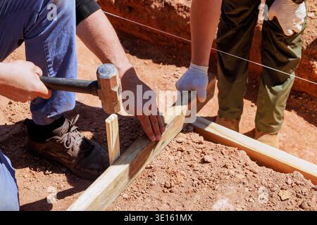 Two workers use hammer wood to set up frame for building foundation in dirt. Stock Photo
