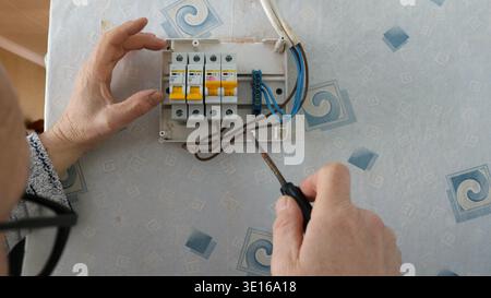 Male hands holding a screwdriver and adjusting the operation of a home electric meter hanging on a wall with old wallpaper, Adjusting circuit breakers Stock Photo