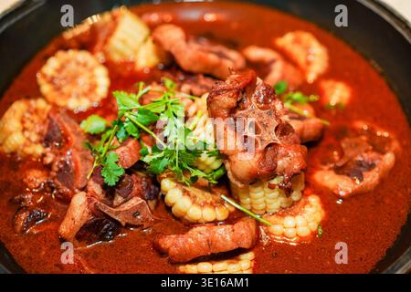 Oxtail stew simmering in a spicy red broth with corn cobs, fresh cilantro, hearty asian comfort dish slow cooked for rich flavor, perfect for cozy Stock Photo