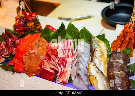 Various cuts of fresh raw meat, seafood, and vegetables arranged on bed of ice and leaves, offering a selection for a hot pot or grill dining Stock Photo