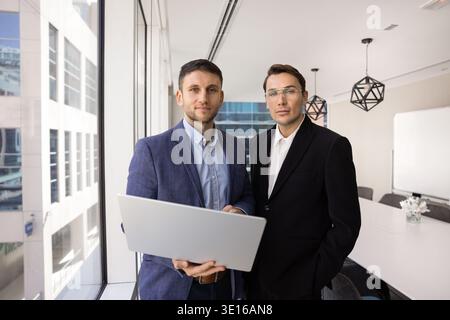 Two businessmen stand in modern office meeting room with laptop Stock Photo