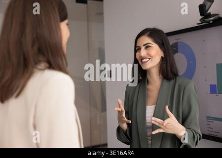 Cheerful Mexican woman explains creative idea during discussion with colleague Stock Photo