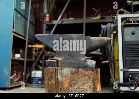 Blacksmith anvil on a wooden stump inside an industrial workshop, highlighting metalworking craft, repair capability and fabrication workspace Stock Photo
