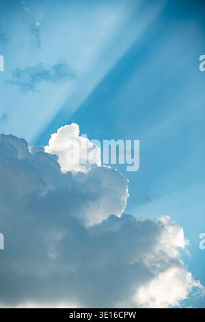 Blue sky background with white cumulus clouds, bright sunbeams streaking through Stock Photo