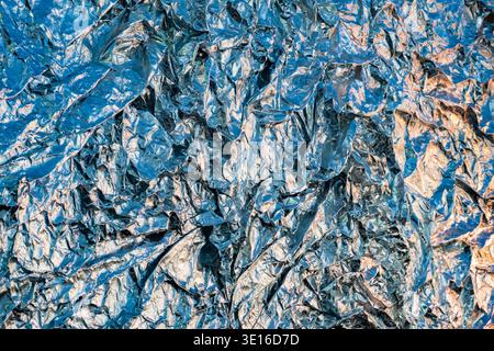 Crumpled aluminum foil texture creating an abstract metallic background with blue light Stock Photo