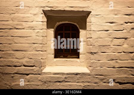 Arched wooden window set in a textured, illuminated brick wall at night Stock Photo