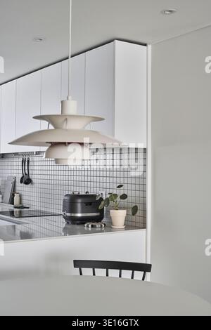 Minimal white kitchen corner with pendant light and cooktop. Stock Photo