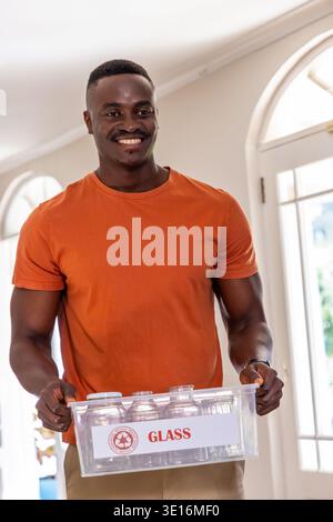 African American adult man standing in foyer in orange tee holding clear GLASS crate Stock Photo