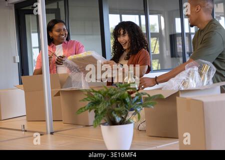 Diverse coworkers unpacking cardboard boxes at modern office desk with bubble wrap and lamp Stock Photo
