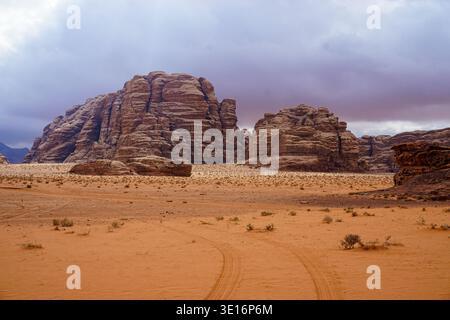 Sandstone rock formations rising from desert landscape under cloudy sky in Wadi Rum desert, Jordan. Stock Photo