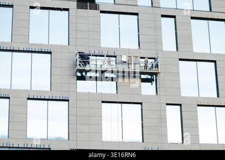 Construction workers are actively engaged in installing exterior panels on a high-rise building using a suspended platform, showcasing urban developme Stock Photo