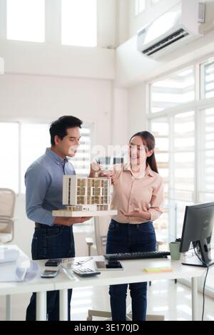 Asian architects collaborating on building design project reviewing model in modern office. Professional team discusses urban development plans for fu Stock Photo