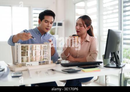 Asian architects engage in serious discussion examining building model detailing plans for future construction project professional design studio meet Stock Photo