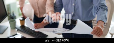 Adult construction experts examine detailed plans discussing project strategies at professional office workplace showing collaboration Stock Photo