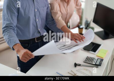 Two professionals examine architectural drawings discussing building project details in a contemporary office setting collaboration planning construct Stock Photo