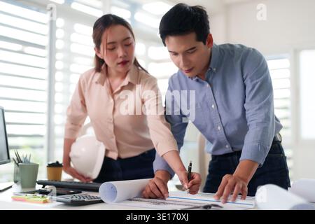 Two professional Asian designers discussing architectural plans. They collaborate on a new building development project vision. Stock Photo