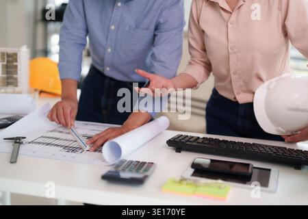 Adult construction professionals examine blueprints and discuss plans for a building project in a modern office environment Teamwork and design develo Stock Photo