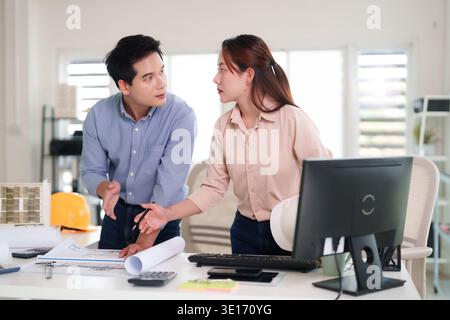 Asian adult architects engineers collaborating on complex building blueprints and a structural model in a bright modern office environment Stock Photo