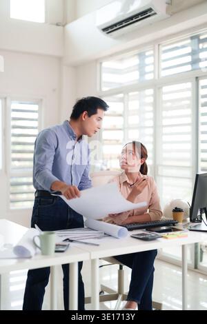 Professional Asian team collaboration reviewing architectural blueprints design solutions Engineers discussing project development in bright office en Stock Photo