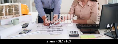 Adult Asian architects engineers meticulously review building plans collaborating on new construction project design at office desk planning developme Stock Photo