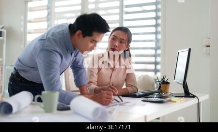 Adult Asian colleagues professionals focus on architectural blueprints planning future project design discussing engineering work solutions Stock Photo
