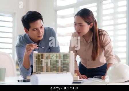 Professional Asian architects collaborate reviewing an architectural model in a modern office. They discuss urban planning and creative design solutio Stock Photo
