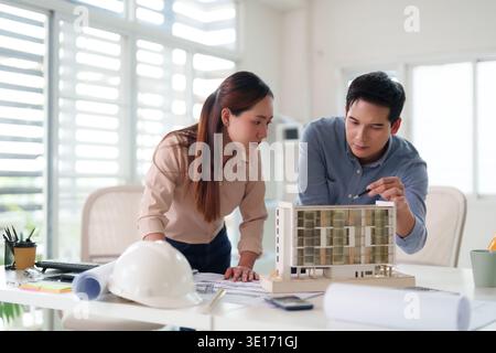 Two dedicated professionals intently examine an architectural model and plans fostering creative solutions for future construction projects. Stock Photo