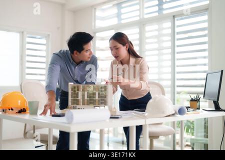 Professional Asian architects collaboratively reviewing new architectural design blueprints and an innovative building model during an office meeting Stock Photo