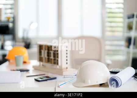 Architectural model hard hats blueprints calculators rulers on clean white desk blur background office environment design planning engineering safety Stock Photo
