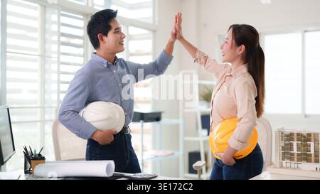 Adult Asian engineers architects collaborating achieving success celebrating project milestones with high five in bright modern office Stock Photo