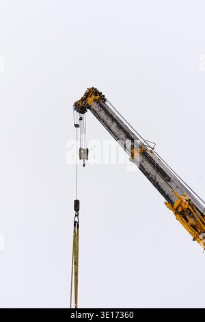 A construction crane arm with cables and hook extends upward against a pale overcast sky Stock Photo