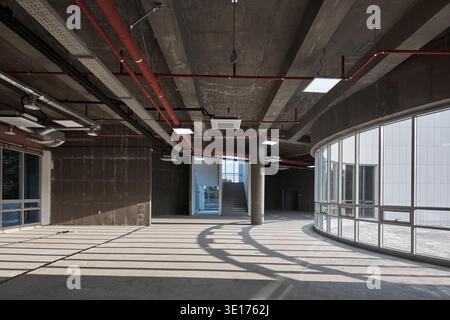 Unfinished concrete interior with dramatic sunlight and curved glass wall. Stock Photo