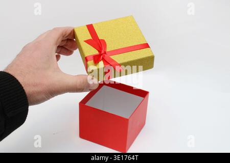 Hand opens the box against a clean white background. Red interior contrasts with shiny exterior. Simple, elegant, festive gesture for any occasion Stock Photo
