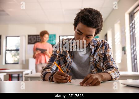 Diverse teacher and student collaborating in classroom with writing in notebook and holding tablet. Education, learning, literacy, mentorship, hallway, knowledge, study || Model released Stock Photo