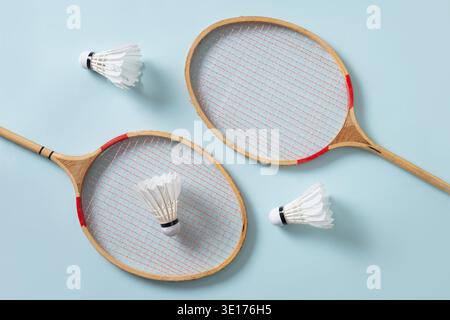 Two wooden badminton rackets and white feather badminton shuttlecocks on green background. View from above. Sport background. Concept racket sport. Leisure games. Stock Photo