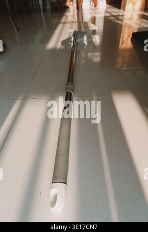 Long-handled mop with gray grip lying on glossy tiled floor in modern home interior Stock Photo
