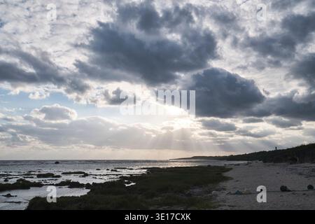 Sunbeams breaking through clouds above the rocky shore. Stock Photo