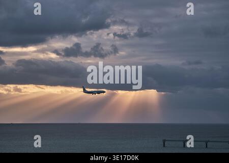 Sun rays over the sea with a distant airplane crossing the horizon. Stock Photo