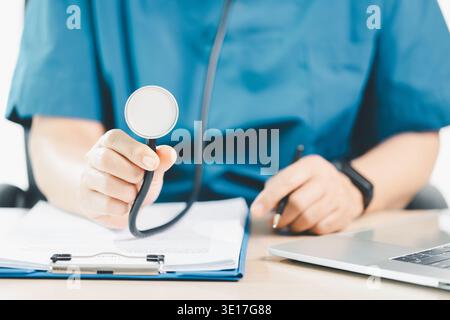 Medical professional in blue scrubs using tablet and stylus with stethoscope, documenting patient records at clinic desk, concept of digital health, t Stock Photo