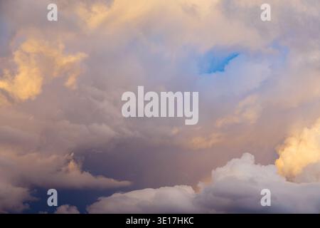 A dramatic and expansive sky filled with fluffy, colorful clouds tinted with soft hues of pink and gold, creating a serene and picturesque sunset atmo Stock Photo