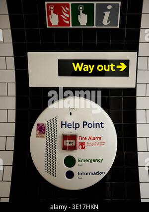 Round sign shows emergency and information services. Wall-mounted unit for safety, public transport, or commercial use. Yellow arrow indicates exit di Stock Photo