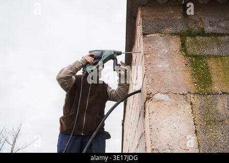 A construction worker operates a powerful rotary hammer drill to penetrate a sturdy concrete wall. The image captures a moment of intense focus in a c Stock Photo