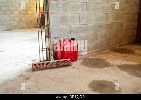A corner of a construction site features a red fuel container and broom against a concrete block wall. The clean, open space highlights the site's rea Stock Photo