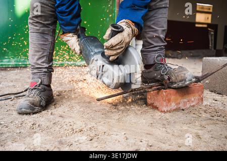 A construction worker skillfully operates an angle grinder, cutting through a metal bar. Sparks fly as the tool makes contact, showcasing the intensit Stock Photo
