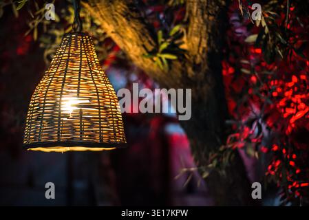 An intricately woven bamboo lampshade casts a warm, golden glow on a tree, enlivened by vibrant colors, capturing the enchanting atmosphere of Marrake Stock Photo