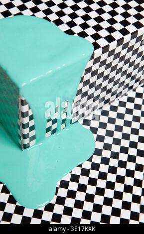 A cube with black and white checkered pattern is drenched in vibrant turquoise paint, creating a dynamic and modern pop art scene that highlights cont Stock Photo